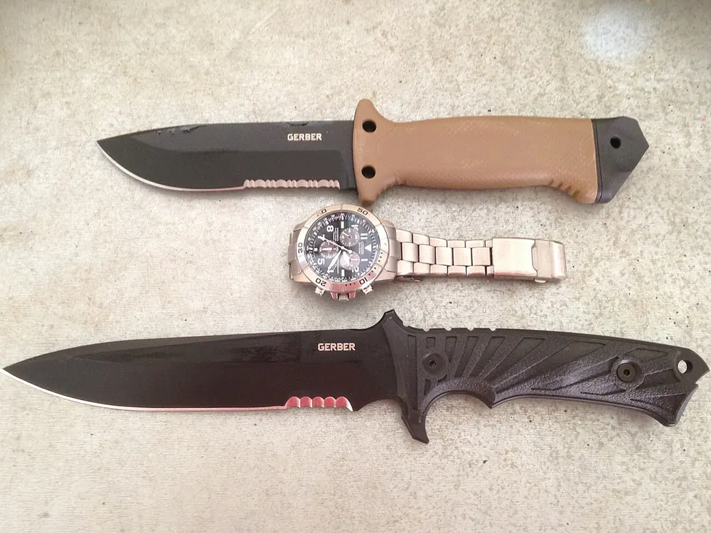 Two survival knives with a watch on a wooden board