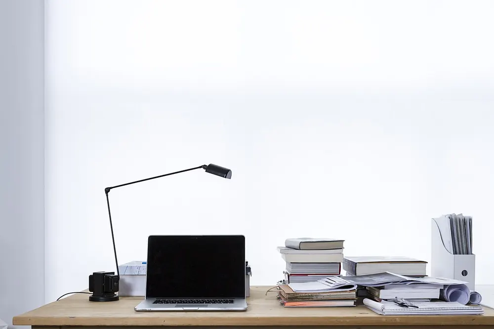 Laptop on a desk next to stacks of books, research before you get hit by a CS2 trading scam